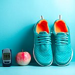 A blood glucose monitor, an apple, and running shoes on a blue background
