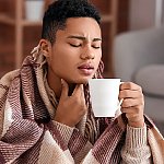 A man holding his throat in pain and drinking a cup of tea