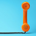 An orange telephone with a black coil cord on a blue background