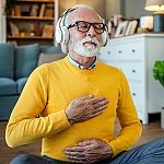 A senior man meditating at home with headphones on