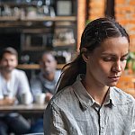 An upset young woman sitting alone with two friends in the background