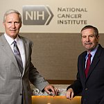 John T. Schiller and Douglas R. Lowy standing in front of the NCI logo