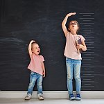 Two children sisters play together. Kid measures the growth on the background of blackboard. Concept of education.