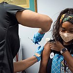 Healthcare worker administers a vaccine to upper right arm of seated volunteer.