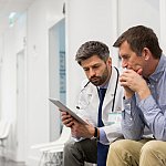 Mid adult doctor explaining serious patient over digital tablet at hospital