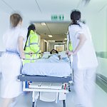 A motion blurred photograph of a child patient on stretcher or gurney being pushed at speed through a hospital corridor by doctors & nurses to an emergency room