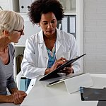 A female doctor sits at her desk and chats to an elderly female patient while looking at her test results