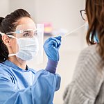 Medical staff worker wearing protective equipment takes sample from nose of another person.