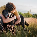 Image of a man in a grassy field hugging his dog