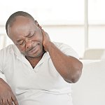 Elderly african man suffering from neck pain at home on couch. Males sense of fatigue, exhausted, stressed. African man massages her painful neck with her hands. The concept of body and health.