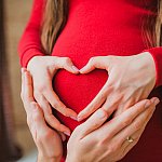 pregnancy concept - couple making a heart shape with their hands on the pregnant belly