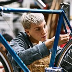 A young adult employee in a bike shop tightens the brakes on the back wheel of a road bicycle.