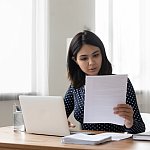 Attentive millennial asian female holding paper letter document reading financial statement. Focused vietnamese business woman worker employee review offer proposal study job contract terms conditions