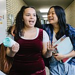 Image of two teenage girls talking and walking together down a classroom hallway during a school day.