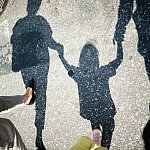 Shadow of two adults walking on a crosswalk and holding hands with a young child in between them.