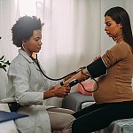 Image of a doctor taking a pregnant patient’s blood pressure.