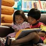 a photo of two preschool-age children looking at a book