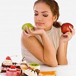 photo of a woman holding two apples but looking down at some sweets