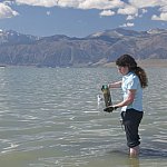 Photo of a woman standing in shallow water with a specimen jar