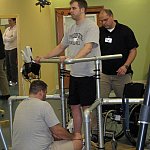 Photo of a standing man supported by hand rails and physical therapists
