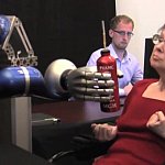 A woman controlling a robotic arm to grasp a bottle.