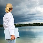 Woman with a laptop looking over a lake as a heavy storm approaches.