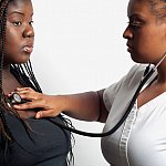 Doctor using a stethoscope to examine an overweight African-American woman.
