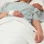 Heath care worker placing a hand on the shoulder of a sick patient in bed
