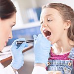 Woman doctor examining girl’s throat with spatula and flashlight