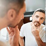 Mature man looking in bathroom mirror at the gray hair in his beard