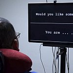 Rear view of man with an electrode array in his head watching a screen with words.