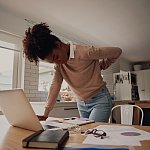 Young woman standing and holding back while working on laptop at home