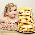 Young girl licking her lips and eying a huge stack of pancakes