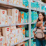 Mother picking out diapers at a store with a baby in a sling