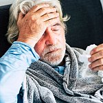 Older man holding his head with one hand and a tissue in the other