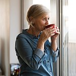 Senior woman looking out a window sipping a cup of tea