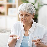 Senior woman taking pills with glass of water at home