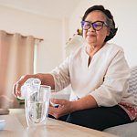 Senior woman pouring water into a glass to drink