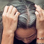 Top view of woman holding gray hair with both hands.