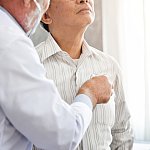 Doctor listening to older patient’s chest with stethoscope.