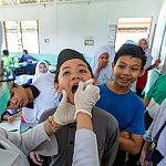 Nurse in a classroom setting giving smiling children an oral vaccine.