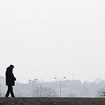 Silhouette of elderly man walking alone outside a city on a hazy, polluted day.