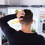 Rear view of a confused man looking at food in refrigerator.