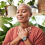 Young black woman meditating among plants indoors.