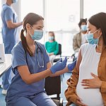 Pregnant woman in face mask receiving a vaccine.