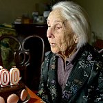 Woman blowing out one hundred candle on her birthday cake.