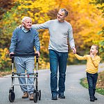 Elderly father with adult son and grandson out for a walk in the park.