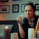 Woman on a couch grimacing at the taste of a drink she has mixed.