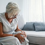 Senior woman on a couch holding her knee in pain.
