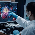 A researcher pointing to a molecular structure on a computer monitor.
